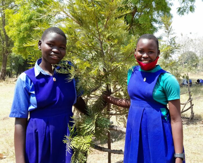 Environmental club members Gladys (left) and Phiona (right) at their school with a tree they planted. Photo by Godfrey Zaake.